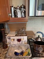 Photo showing French presses, tall wooden pepper grinder, glassware, and disposable tray with small glass and ceramic items on countertop.