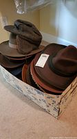 Box with several hats visible including wool fedoras and tweed newsboy cap