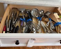 Drawer with assorted kitchen utensils including wooden spoons, metal strainers, spatulas, ladle, and tongs.