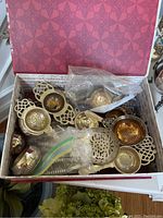 Top view of multiple silver plated and metal tea brewing strainers and caddies inside decorative box