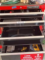 Red Craftsman tool chest with three drawers partially open, showing a yellow DeWalt drill in soft carry bag and various hand tools inside drawers, on a large garage floor.