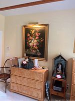 View of the framed floral painting hanging above a dresser, showing the surrounding furniture and room context.