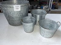 Large galvanized buckets with embossed floral design and handles alongside smaller plain galvanized buckets.