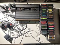 Overview of Atari 2600 console, controllers, paddles, power adapter and stacked game cartridges on table