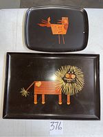 Top view of two black wood embossed Couroc trays, one large rectangular with a lion pattern and one smaller rectangular with a bird pattern