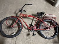 Full side view of red cruiser bike showing frame, tires, handlebars, seat, pedals, and rear cargo rack