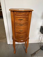 Front view of the tall wooden jewelry armoire showing its four curved front drawers with decorative handles and carved details on the legs and trim.