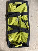 Top view of large green and black LL Bean duffel bag with black straps, showing wear and creases.