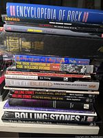 Stack of rock music books including Encyclopedia of Rock, several books about The Rolling Stones, John Lennon, and related titles.
