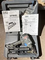 Senco SFN40 pneumatic nailer inside its case along with two instruction sheets placed over the tool.