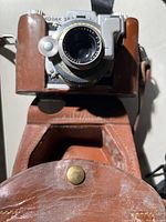 Kodak 35 camera in brown leather carrying case, showing lens and front body, leather case worn