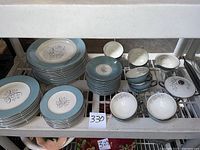 Photo of stacked dinner plates, sandwich plates, dessert plates, cups, saucers, lidded sugar bowl, and creamer showing blue border and floral design.