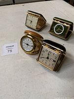Four vintage travel clocks arranged on flat surface showing various designs and cases.