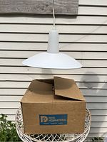 White vintage hanging lamp suspended over its original box labeled 'Revel International'. The lamp has a wide, flared shade and conical top fitting attached to electrical cord.