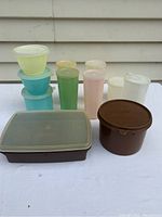 Full view of 10 vintage Tupperware containers in pastel colors with lids, showing various shapes and sizes including round, tall cylindrical, and rectangular containers.