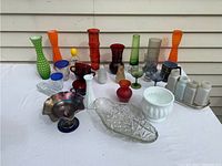 Photo showing assortment of colorful glassware including hobnail milk glass vases, carnival glass vases in red, amber, green, clear cut crystal dish, white milk glass planter, and a set of four white ceramic salt and pepper shakers.
