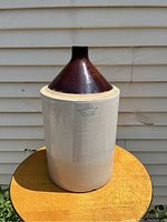 Side view of jug showing off-white lower body and brown conical glazed top, sitting on wooden surface against a siding wall.