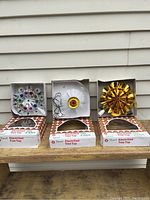 Three vintage Christmas tree toppers in original boxes on wooden surface against siding background
