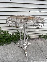 Side perspective of the white metal wire filigree garden table showing the decorative base and round top with rust spots.
