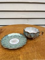 Teacup and saucer placed on wooden table showing side view highlighting the cup's faceted design and luster glaze
