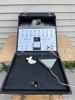 Front view of the DuKane electronic programmer with the front panel opened, showing the switches, meter, and foot pedal on a wooden table.