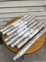 Seven rolls of floral wallpaper arranged on a round wooden table, showing condition and packaging.