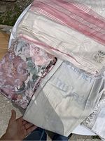 Photo showing the IBEX flannel sheet in clear original packaging with red stripes, and various folded linens including hand embroidered cloth and floral fabric.