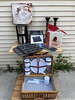 Photo showing entire assortment on wooden shelves, including coffee maker, muffin pans, Henckels cutting tools box, wicker picnic basket with plates and mugs, tall candlesticks, and boxed salad servers.