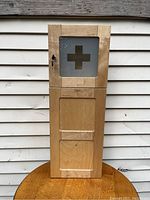 Front view of the hardwood medicine cabinet showing frosted glass door with cross and lower wooden panels.