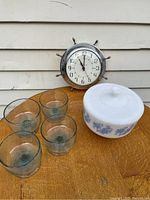 Full lot arranged on wooden table against siding, showing the clock, covered dish, and four green glass bowls.
