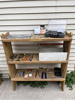 Wooden shelf with various used hand tools, including clamps, pliers, soldering kit, wrenches, and other small tools arranged on three shelves.