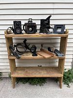 Wide shot of wooden shelving displaying an assortment of vintage photographic and aircraft camera equipment including camera frames, exposure timer, lens attachments, and various mechanical parts.