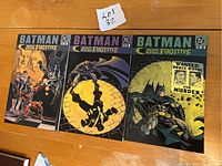 Front covers of Batman Bruce Wayne: Fugitive Volumes 1, 2, and 3 laid flat on a wood surface.