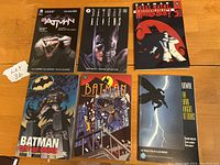 Front covers of six Batman graphic novels laid out on a wooden surface.