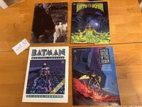 Four Batman graphic novels displayed on a wooden surface showing front covers.