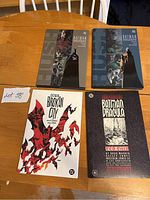 Four Batman graphic novels on a wooden table including two Batman: Hush volumes, Broken City, and Batman/Dracula Red Rain.