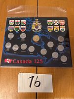 Framed set of Canadian coins displayed over a blue map background with provincial crests and Canada 125 emblem