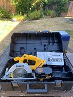 Full view of DeWalt circular saw, battery, manual and molded black carrying case on outdoor surface.