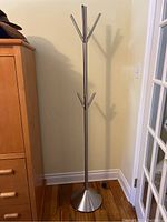 Full view of the metal coat rack standing next to a wooden dresser showing its height and structure