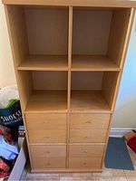 Front view of the pine colored IKEA pantry cabinet with four open cubby shelves on top and eight drawers below.