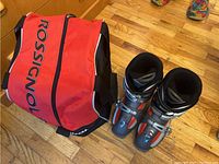 Photo showing the red and black Rossignol branded carrying bag alongside the pair of black, gray, and red Head ski boots.