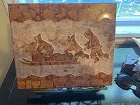 Photo of front view of marble stone carving showing Inuit figures on sled with dog and walking figure