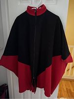 Front view of black and red women's wool cape hanging on door, displaying full length and zipper.