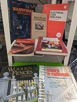 Photo showing 7 of the home and garden books standing on a mesh chair including handyman guide, barn plans, electrical code, furniture, wooden fences, and stairs & railings books.