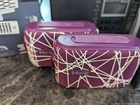 Two purple iHome Bluetooth speakers with white abstract line pattern placed side by side.