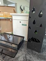 Photo of black horizontal metal mailbox, white vertical mailbox in background, and black metal umbrella holder with cut-out design