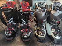 Front view of two pairs of ski boots. Left pair is red and black Dragon ski boots. Right pair is white and black Salomon ski boots.