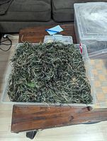Ghillie suit laid out in storage container showing thick synthetic jute camouflage threads in green, tan, and brown over camouflage fabric base.