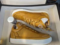 Pair of yellow leather sneakers labeled 'Smooth Mimosa' shown inside open shoebox with accompanying shoe care product container.