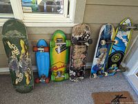Photo showing six skateboards lined up including Anti-Hero deck, blue banana board, green Rumble board, two skate park boards, and longboard with Surf's Up motif.